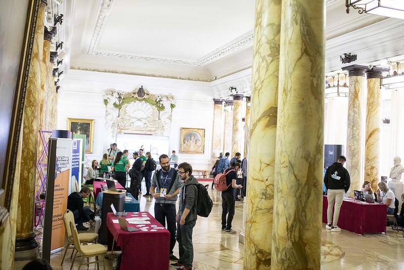 Looking down room with tables along either side. The tables have branding from various companies.